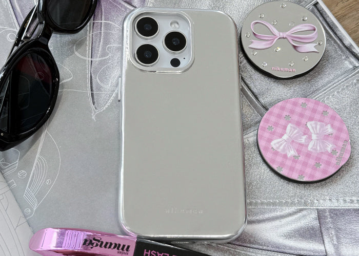 Silver phone case on a surface with sunglasses, pink items, and decorative coasters.